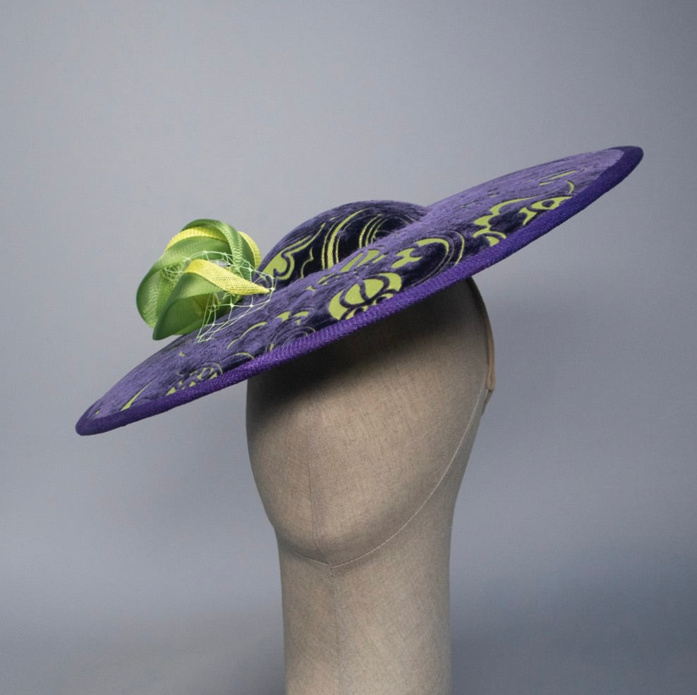 Purple decorative hat with green accents on a mannequin head against a gray background