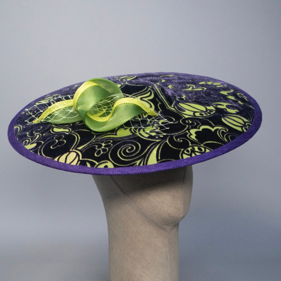 Purple hat with green decorative bow on a mannequin head against a gray background