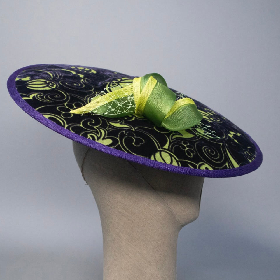 Purple decorative hat with green trim on a mannequin head against a gray background