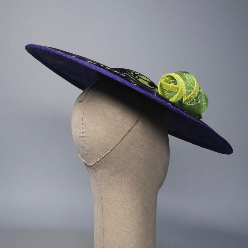 Purple hat with green decorative element on a mannequin head against a gray background