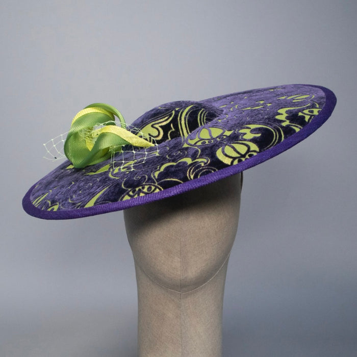 Purple decorative hat with green accents on a mannequin head against a gray background